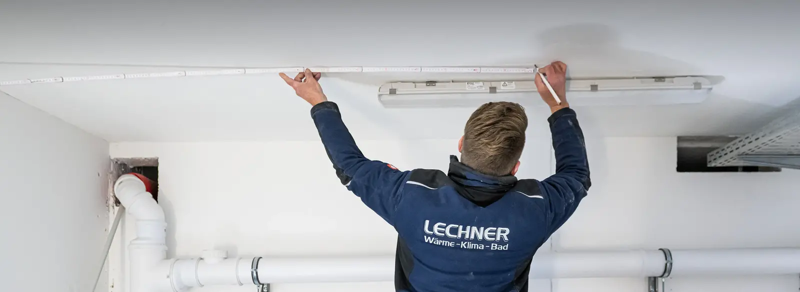 Ein Techniker in hochwertiger, CI-gerechter Berufskleidung des Unternehmens Lechner führt Montagearbeiten durch. Durch moderne und funktionale Arbeitskleidung zeigt das Unternehmen Wertschätzung für seine Mitarbeiter und stärkt seine Position im Wettbewerb um Fachkräfte. Der DBL Mietservice übernimmt die Pflege der Kleidung und entlastet so die Mitarbeiter im Alltag.